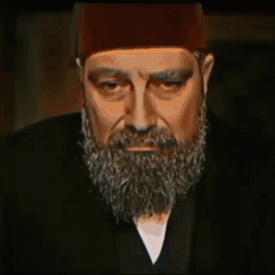 A Man With A Beard Wearing A Hat And A Black Jacket GIF