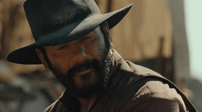 A Man With A Beard Wearing A Hat And A Brown Shirt GIF