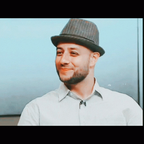 A Man With A Beard Wearing A Hat And A Striped Shirt GIF