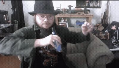 A Man With A Beard Wearing A Hat And Glasses Is Holding A Bottle Of Bud Light GIF