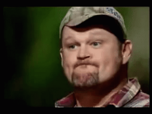 A Man With A Beard Wearing A Hat And Plaid Shirt Is Making A Funny Face . GIF