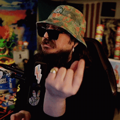 A Man With A Beard Wearing A Hat And Sunglasses Is Sitting In Front Of A Microphone Giving The Middle Finger . GIF