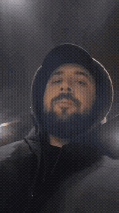 A Man With A Beard Wearing A Hat Covering His Mouth With His Hands GIF