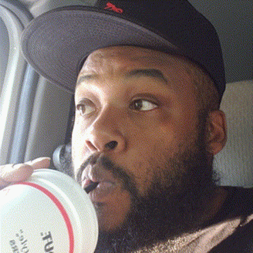 A Man With A Beard Wearing A Hat Is Drinking From A Container That Says ' True ' On It GIF