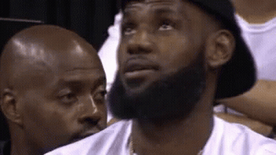 A Man With A Beard Wearing A Hat Is Sitting In A Stadium . GIF