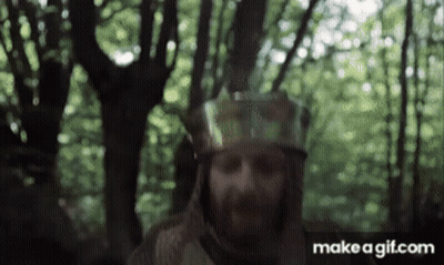 A Man With A Beard Wearing A Helmet Is Standing In A Forest . GIF