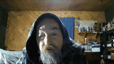 A Man With A Beard Wearing A Hooded Jacket Looks At The Camera GIF