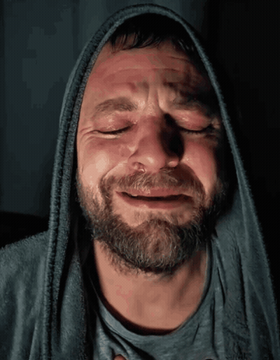 A Man With A Beard Wearing A Hooded Sweatshirt Is Crying With His Eyes Closed GIF