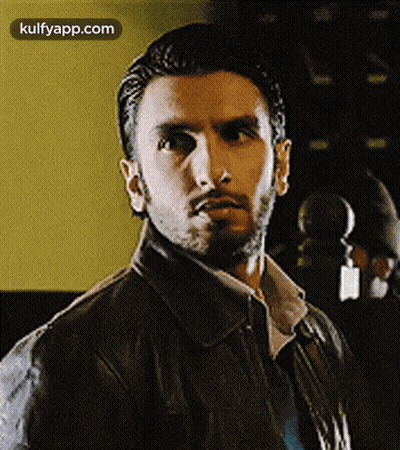 A Man With A Beard Wearing A Leather Jacket And Tie Is Looking At The Camera . GIF