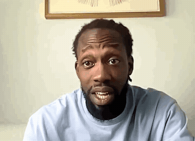 A Man With A Beard Wearing A Light Blue Shirt Looks At The Camera GIF