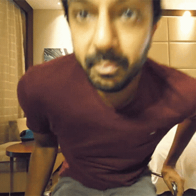 A Man With A Beard Wearing A Maroon Shirt Looks At The Camera GIF