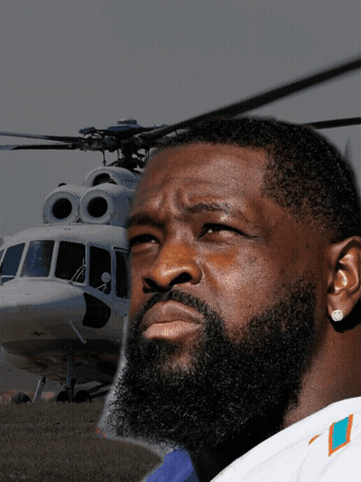 A Man With A Beard Wearing A Miami Dolphins Shirt Stands In Front Of A Helicopter GIF
