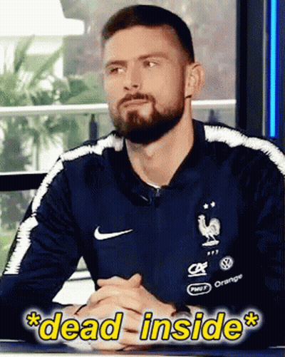 A Man With A Beard Wearing A Nike Shirt Is Sitting At A Table With His Hands Folded GIF