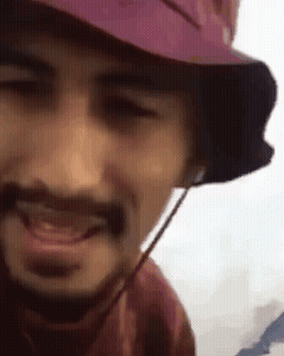 A Man With A Beard Wearing A Pink Hat And Headphones Is Smiling . GIF