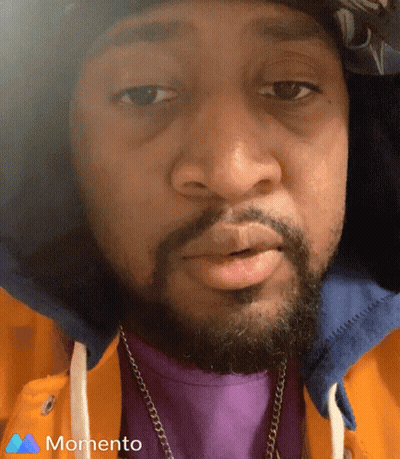 A Man With A Beard Wearing A Purple Shirt And A Momento Logo On The Bottom GIF