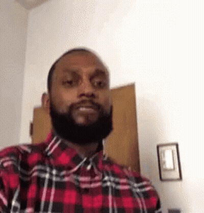 A Man With A Beard Wearing A Red And Black Plaid Shirt Is Standing In A Room . GIF