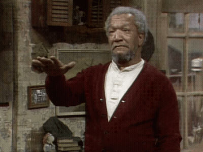 A Man With A Beard Wearing A Red Cardigan Is Standing In Front Of A Window GIF