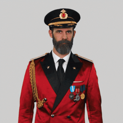 A Man With A Beard Wearing A Red Suit And Black Hat Salutes GIF