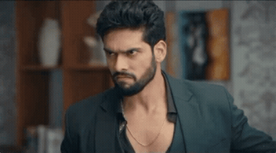 A Man With A Beard Wearing A Suit And A Chain Around His Neck Is Looking At The Camera . GIF