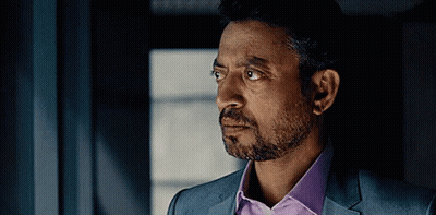 A Man With A Beard Wearing A Suit And A Purple Shirt Is Looking Out A Window . GIF