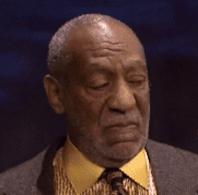 A Man With A Beard Wearing A Suit And Tie Is Making A Funny Face . GIF