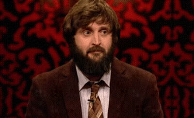 A Man With A Beard Wearing A Suit And Tie Is Standing In Front Of A Red Wall . GIF