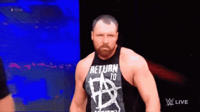 A Man With A Beard Wearing A Tank Top That Says `` Return To Anarchy '' Is Standing In A Dark Room . GIF