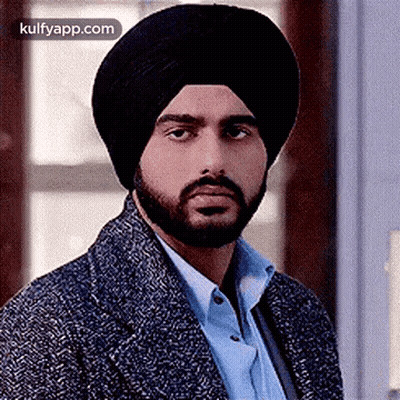 A Man With A Beard Wearing A Turban And A Jacket Is Looking At The Camera . GIF
