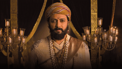 A Man With A Beard Wearing A Turban And Pearls Looks At The Camera GIF
