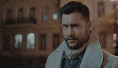 A Man With A Beard Wearing A White Coat And A Turtleneck Sweater . GIF