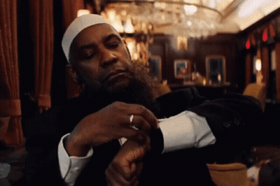 A Man With A Beard Wearing A White Hat And A Black Suit Is Looking At His Watch GIF