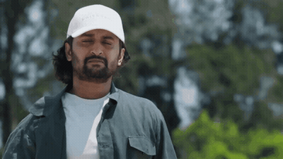 A Man With A Beard Wearing A White Hat And A Gray Shirt . GIF