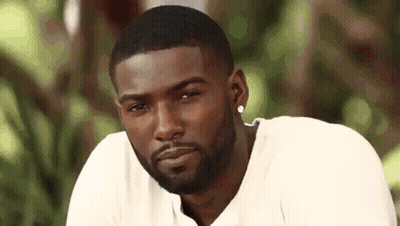 A Man With A Beard Wearing A White Shirt And Earrings Is Looking At The Camera . GIF