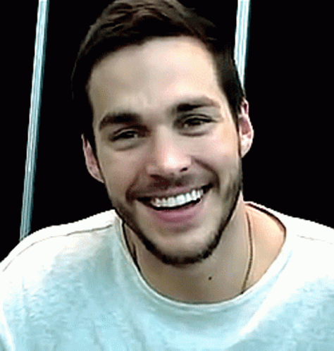A Man With A Beard Wearing A White Shirt Is Smiling For The Camera GIF