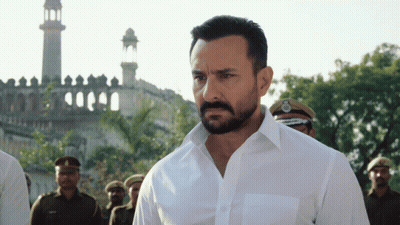 A Man With A Beard Wearing A White Shirt Is Standing In Front Of A Mosque GIF