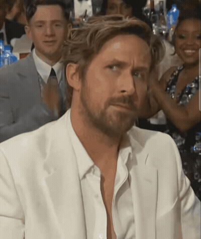 A Man With A Beard Wearing A White Suit Looks At The Camera GIF
