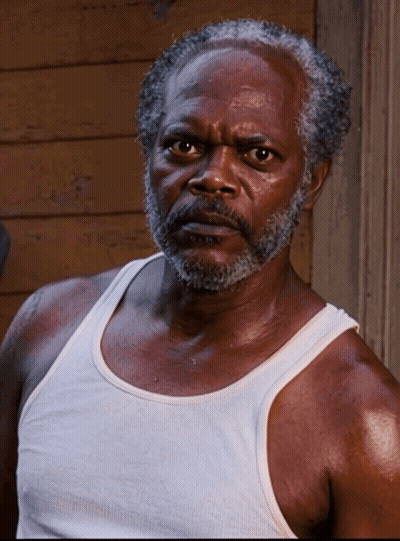 A Man With A Beard Wearing A White Tank Top Looks At The Camera GIF