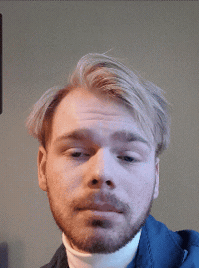A Man With A Beard Wearing A White Turtleneck Looks At The Camera GIF