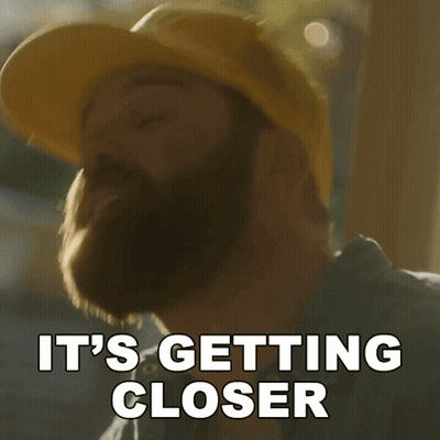 A Man With A Beard Wearing A Yellow Hard Hat Says It 'S Getting Closer GIF