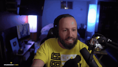 A Man With A Beard Wearing A Yellow Shirt With The Letters Bb On It Is Sitting In Front Of A Microphone GIF