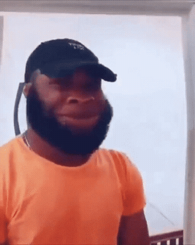 A Man With A Beard Wearing An Orange Shirt And A Black Hat . GIF