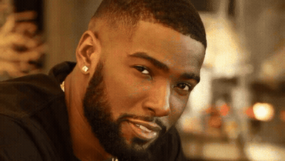 A Man With A Beard Wearing Earrings And A Black Shirt GIF