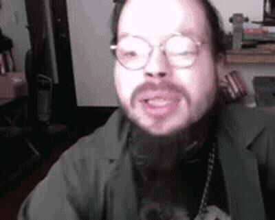 A Man With A Beard Wearing Glasses And A Green Jacket Is Talking . GIF