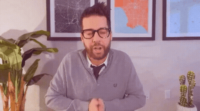 A Man With A Beard Wearing Glasses And A Grey Sweater And Tie GIF