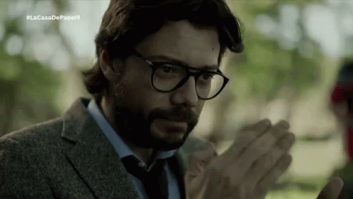 A Man With A Beard Wearing Glasses And A Suit Is Clapping His Hands . GIF