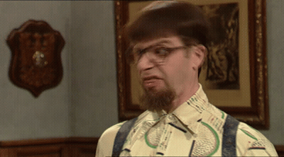 A Man With A Beard Wearing Glasses And Suspenders Looks At The Camera GIF
