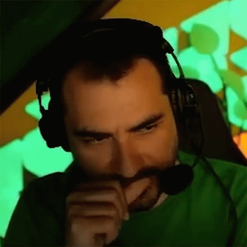 A Man With A Beard Wearing Headphones And A Green Shirt Is Sitting In A Chair . GIF