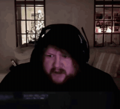 A Man With A Beard Wearing Headphones And A Hooded Jacket Is Laying In A Bed . GIF