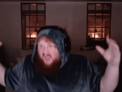 A Man With A Beard Wearing Headphones And A Hooded Shirt Is Dancing In A Dark Room . GIF