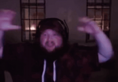A Man With A Beard Wearing Headphones And A Hoodie Is Dancing In A Dark Room GIF